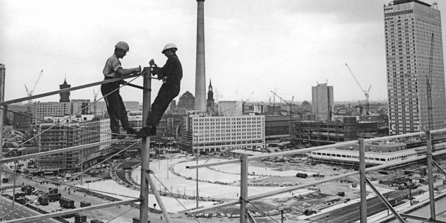 Photo of construction workers at a vertiginous height atop the Haus der Statistik, in the background the TV tower